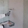 Applicazione a rullo di aggrappante quarzato su calcestruzzo liscio prima dell’intonaco