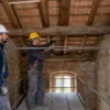 Tecnici installano una catena antisismica con tenditore tra due muri in pietra