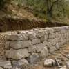 Muro a secco in pietra con fondazione, scarpa e riempimento drenante durante la posa