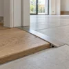 Profilo di raccordo in alluminio tra parquet in rovere e piastrelle grigie di gres in un vano porta