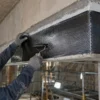 Operatore con DPI applica un tessuto CFRP in fibra di carbonio su una trave in calcestruzzo