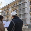 Illustrazione di un condominio con lavori in corso e due persone che esaminano documenti tecnici
